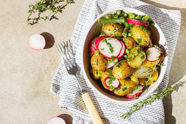 Tasty hot potato salad with green beans, fresh radishes and herbs dressing with olive oil and mustard sauce, light concrete background. Top view. stock photo