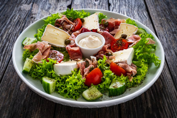 Tasty salad - ham, brie cheese and fresh vegetables on wooden table stock photo