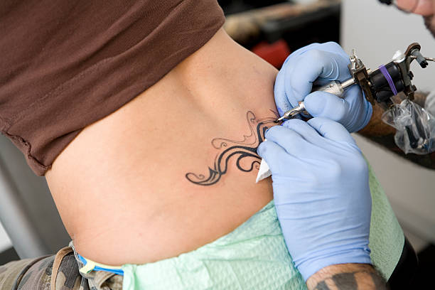 artista de tatuagem trabalhando em uma tatuagem - lombar - fotografias e filmes do acervo