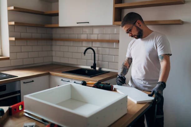 A tattooed worker is setting up a drawer in his kitchen. He is using a pencil to mark the wooden material. stock photo