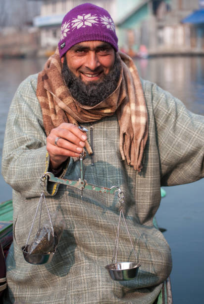 Tea seller wearing pheran on Dal Lake, Kashmir, India weighs a bag of tea while in his boat stock photo