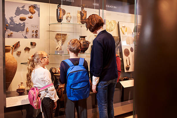 Teacher And Pupils Looking At Artifacts On Display In Museum Teacher And Pupils Looking At Artifacts On Display In Museum museum stock pictures, royalty-free photos & images