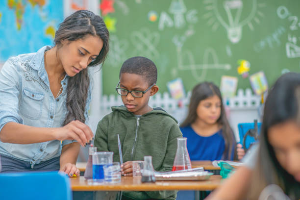 Teacher helping a young boy with chemistry A young female teacher helps a boy in her class to conduct a chemistry experiment. middle school teacher stock pictures, royalty-free photos & images