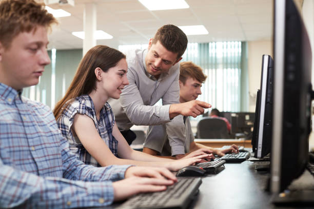 Teacher Helping Female High School Student Working In Computer Class stock photo