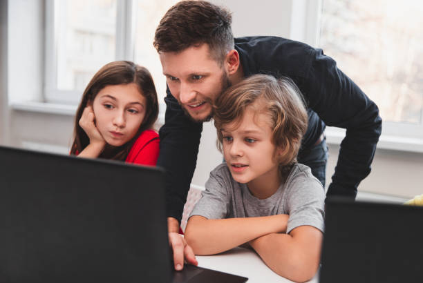 Teacher helping pupils during programming lesson Smart elementary schoolkids with male teacher looking at laptop screen with interest while testing program during lesson in classroom of modern school programming languages to teach kids stock pictures, royalty-free photos & images