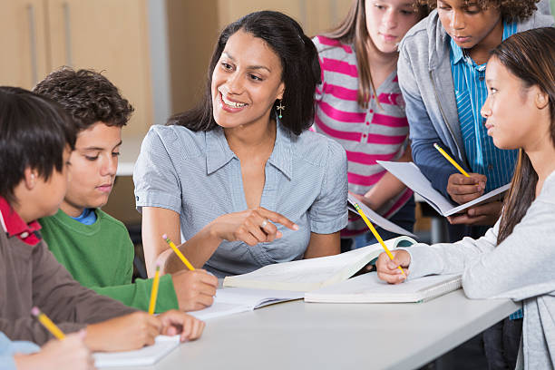 Teacher helping students in classroom Multi-ethnic group of students with teacher in classroom. middle school teacher stock pictures, royalty-free photos & images