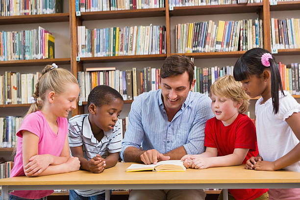 Teacher reading book to pupils at library stock photo