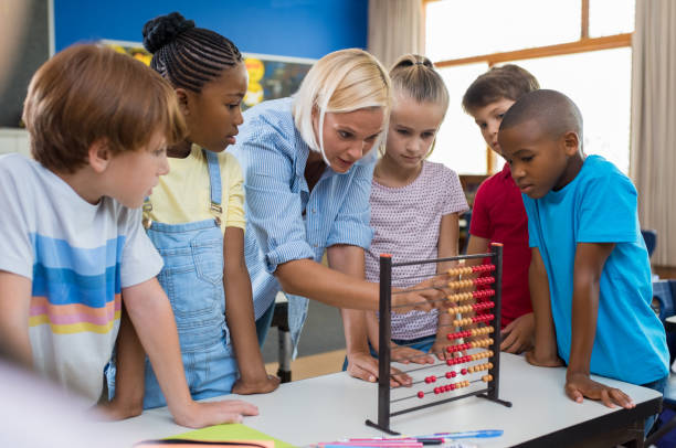 Teacher showing abacus to children Teacher teaching children math on abacus. Mature mathematics teacher helping schoolchildren use wooden abacus. Group of multiethnic kids understanding maths in classroom. abacus stock pictures, royalty-free photos & images