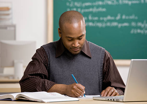 Teacher with laptop computer writing at his desk stock photo
