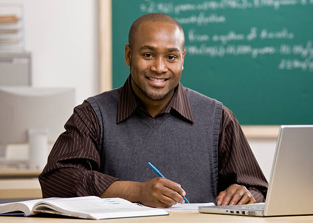 Teacher with laptop grading papers in school classroom stock photo