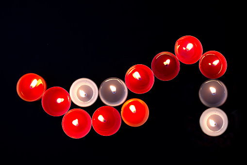 Diverse coloured tea lights  next to each other form the shape of a shoe , on black background