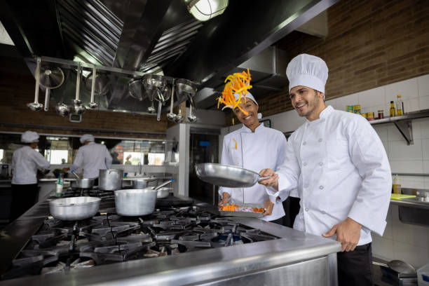 team of latin american chefs cooking together and sautéing some vegetables in a pan while smiling - gesmeten cursus stockfoto's en -beelden