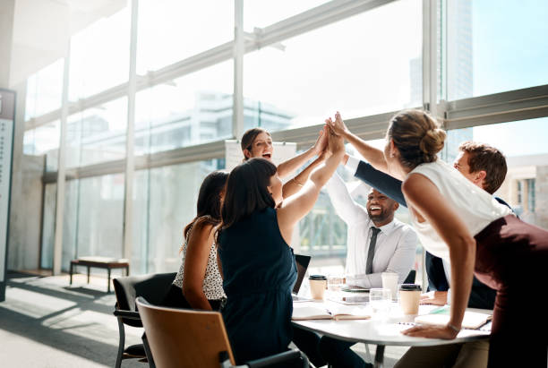 Teamwork always get it done! Shot of a group of businesspeople high fiving while sitting in a meeting business stock pictures, royalty-free photos & images