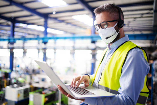 Technician or engineer with protective mask and laptop working in industrial factory. Side view of technician or engineer with protective mask and laptop working in industrial factory. slovakia photos stock pictures, royalty-free photos & images