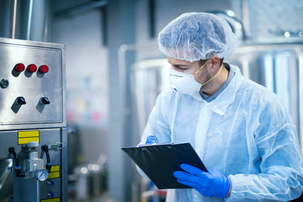 technologist expert in protective uniform with hairnet and mask taking parameters from industrial machine in food production plant. - food imagens e fotografias de stock