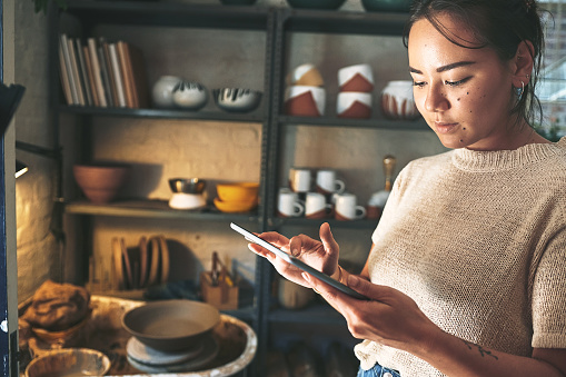 Cropped shot of an attractive young business owner standing alone in her pottery studio and using a tablet