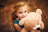 Shot of a happy little girl looking at the camera and holding her teddy bear while standing outside in the woods