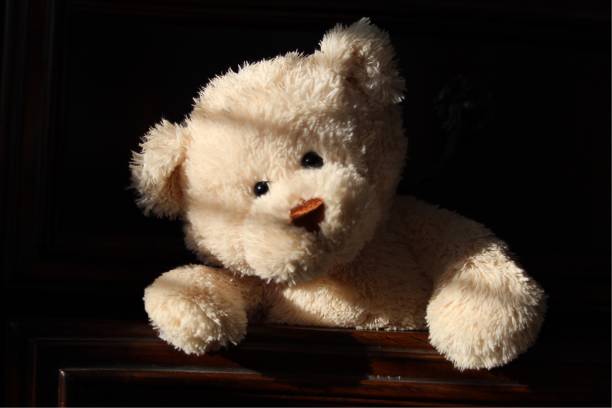 Teddy bear in a drawer Teddy Bear hiding in a dresser drawer.  Sunlight rays on bear.  Black background teddy ray stock pictures, royalty-free photos & images