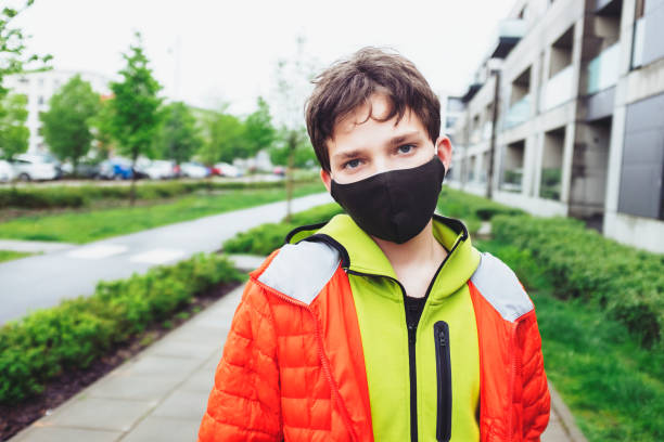 de jongen van de tiener tijdens covid-19 pandemie die zich op een straat met een beschermend handgemaakt gezichtsmasker bevindt op het bekijken van camera die vermoeid en ongerust - taille omhoog dichte omhoog zicht is. - alleen één tienerjongen stockfoto's en -beelden