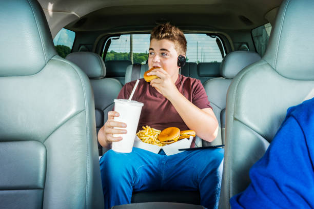 een tiener jongen eten van een hamburger en frietjes nemen op de achterbank van een auto - frietwagen stockfoto's en -beelden