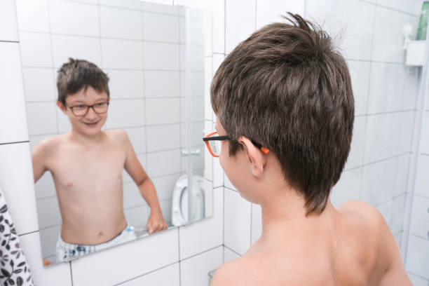 A teen boy looking in a mirror in bathroom and showing muscules stock photo