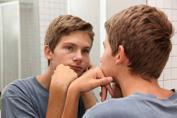 Teen boy looking in mirror with bored expression stock photo