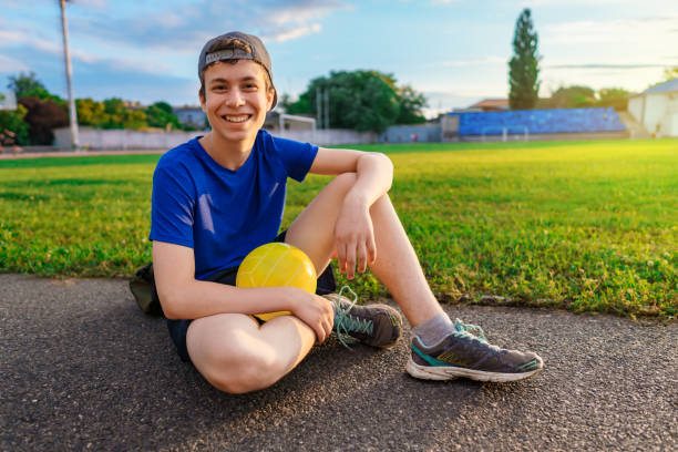 teen boy posing with ball at a stadium, a soccer field with green grass - sports and health concept stock photo