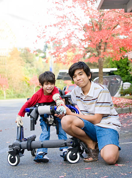 Teen boy with disabled little brother in walker stock photo