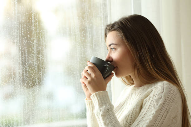Teen drinking coffee looking through a window a rainy day Side view portrait of a relaxed teen drinking coffee looking outside through a window in a rainy day of winter at home tea hot drink photos stock pictures, royalty-free photos & images
