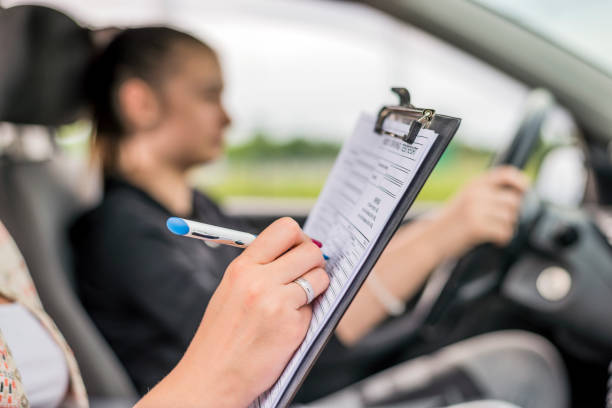Teen getting a driving lesson in the car Teen Girl Learns Driver's Education in Car with Adult woman using clipboard, Young Teen Girl Doing Driving Exam with female Examiner while holding Checklist during bright day. driving test nerves stock pictures, royalty-free photos & images