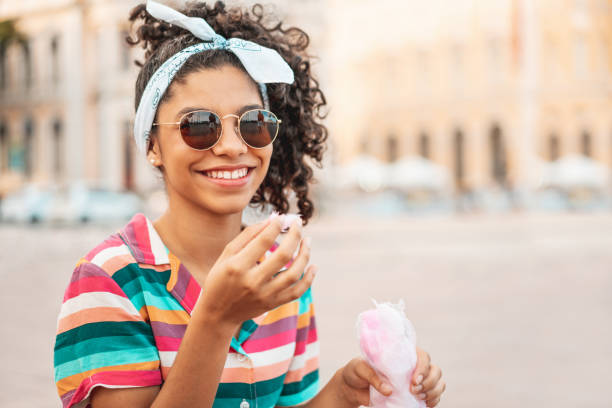 adolescente chica comiendo algodón de azúcar al aire libre - rizado peinado fotografías e imágenes de stock