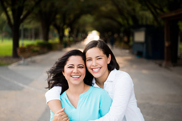 Teen girl embracing mother and smiling at camera A teenage daughter embracing her mother, facing the camera and smiling in a horizontal waist up shot outdoors. mexican teenage girls stock pictures, royalty-free photos & images