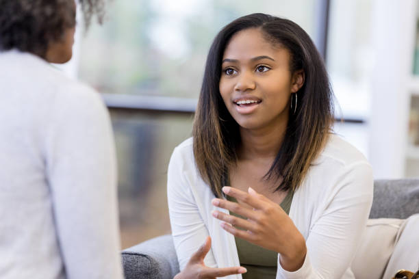Teen girl gestures while talking to unrecognizable counselor Sitting on the couch in the counselor's office, the teen girl gestures as she talks to the unrecognizable female counselor. school counselor stock pictures, royalty-free photos & images