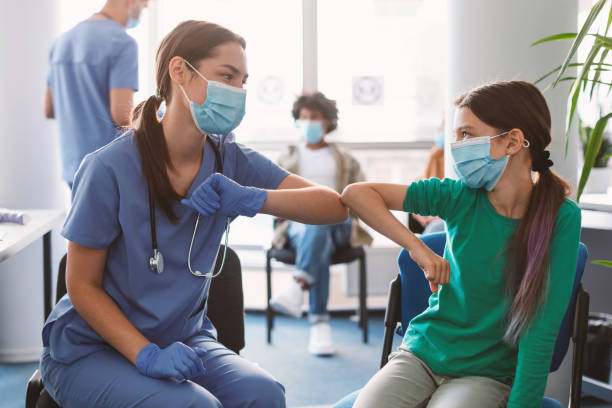 Teen Girl In Medical Mask Bumping Elbows Meeting Female Doctor Elbow Bump Greeting. Teen Girl In Medical Mask Bumping Elbows Meeting Nurse Doctor In Hospital Indoor. Social Distancing And Keeping Safe Distance For Covid-19 Protection Concept pandemic illness photos stock pictures, royalty-free photos & images