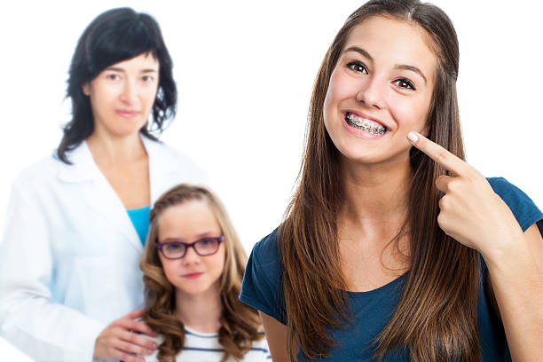 Teen girl pointing at dental barces with doctor in background. stock photo