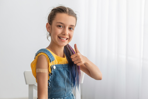 Effective Covid Vaccine Against New Delta Variant. Portrait Of Cheerful Smiling Adolescent Patient Showing Vaccinated Arm With Sticking Patch On Her Shoulder After Getting Shot And Thumb Up Gesture