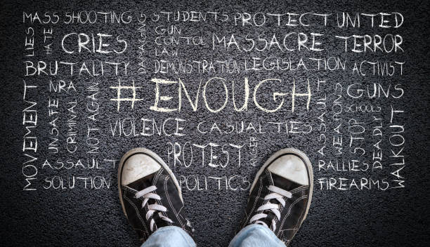 Teen Wearing Canvas Shoes on Asphalt With # Enough Word Cloud A teenager in jeans and canvas shoes standing on asphalt road with # ENOUGH word cloud. Concept of social movement to protest gun violence and mass school shootings in the United States. nra stock pictures, royalty-free photos & images
