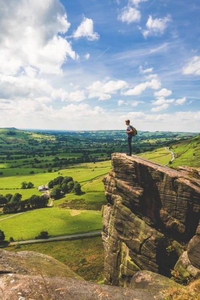 Teenage Boy Stands at Edge in Peak District A teenage boy stands at the edge of a rocky outcropping while rambling along The Roaches in Peak District National Park, United Kingdom. He looks over the rolling green countryside of Staffordshire on a warm summer day. peak district national park stock pictures, royalty-free photos & images