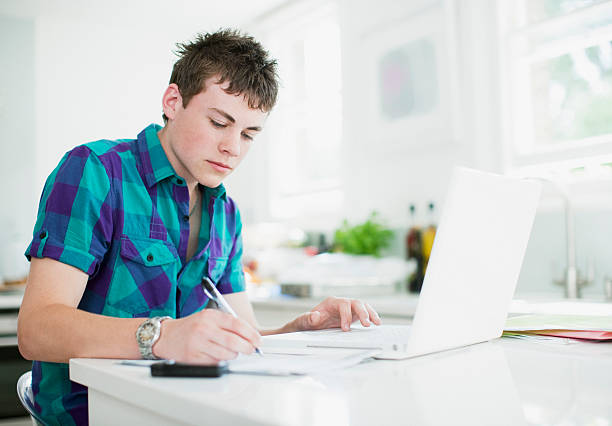 rapaz adolescente usando computador portátil e a fazer trabalho de casa - jovem a escrever imagens e fotografias de stock
