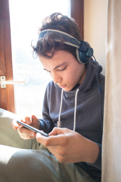Teenage Boy with Headphones Listening to Music on a Smartphone stock photo