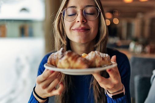 Teenage girl having breakfast in restaurant. She is smelling fresh, warm croissants.
Canon R5