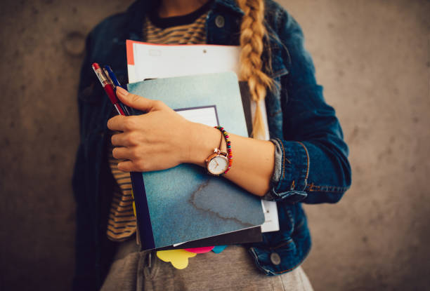 teenage girl holding books, notebooks and pencils standing against wall - school material imagens e fotografias de stock