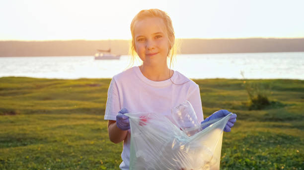Teenage girl looking at the camera holding a bag of collected garbage on the river bank stock photo