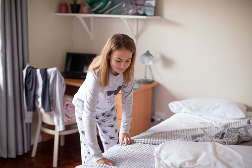 A thirteen-year-old making her bed in her room at home.