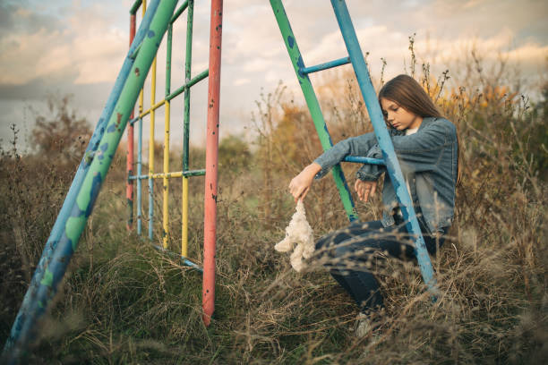 Teenage girl on old abandoned playground Girl sitting on climbing frame on abandoned playground where she grew up on. Grass is overgrown, playground is rusty and broken. There is no children playing on it anymore. She holding teddy bear from her  childhood and looks sad and lonely. broken doll 1 stock pictures, royalty-free photos & images