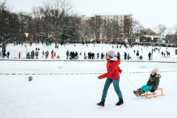 teenage girl pulling little sister on sleigh in public park in berlin street - berlin snow stockfoto's en -beelden