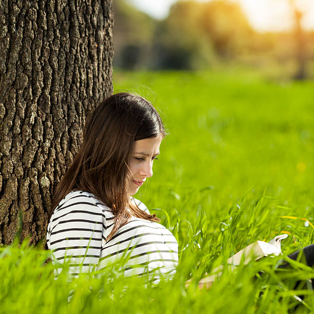 Teenage girl reading book on meadow stock photo