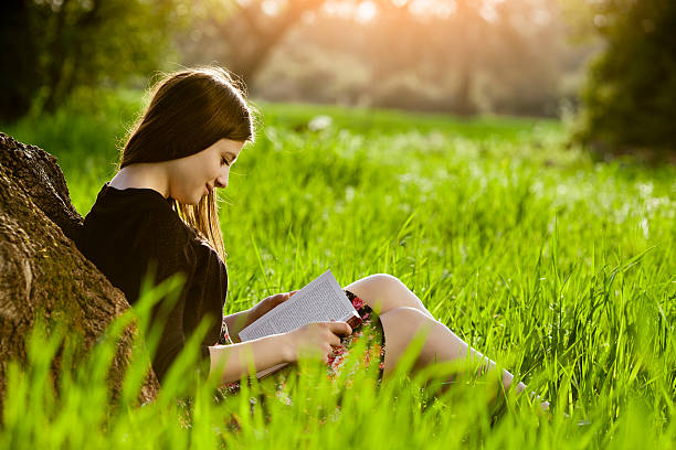 Teenage girl reading book on meadow stock photo
