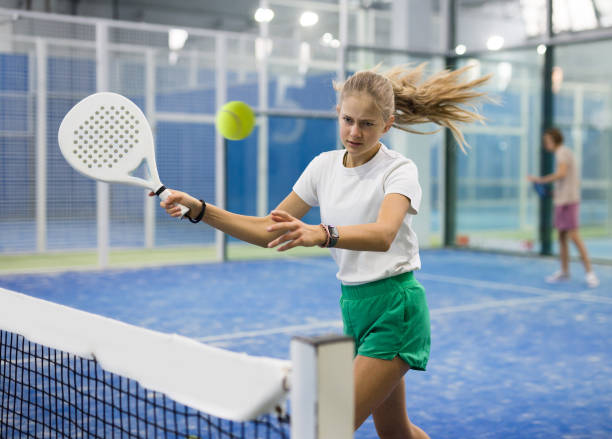 Teenage girl serving ball while playing padel in court stock photo