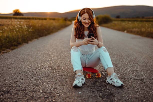 Teenage girl using headphones and smartphone in the street stock photo